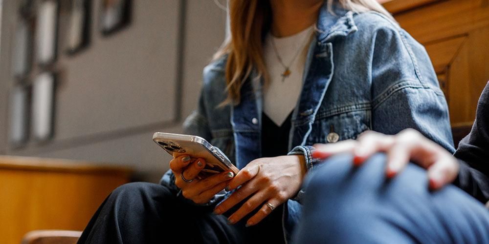 Close up of a student's denim jacket and their hands holding a phone