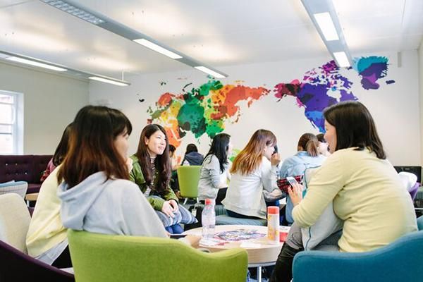 Students socialising in the Global Lounge in the Business School. A large world map is on the wall.
