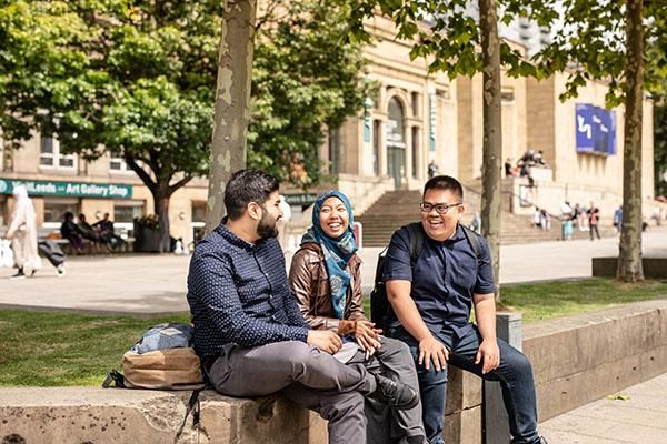Three students sit chatting on a wall outside Leeds Art Gallery