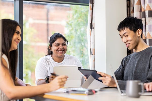 A group of students sitting at a table in university accommodation. They are sitting at a table using tablets.