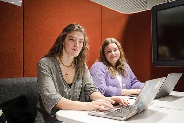 Two students working on laptops sitting in an orange booth