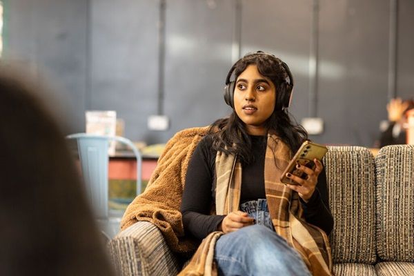 A student sitting in a cafe using their mobile and wearing headphones