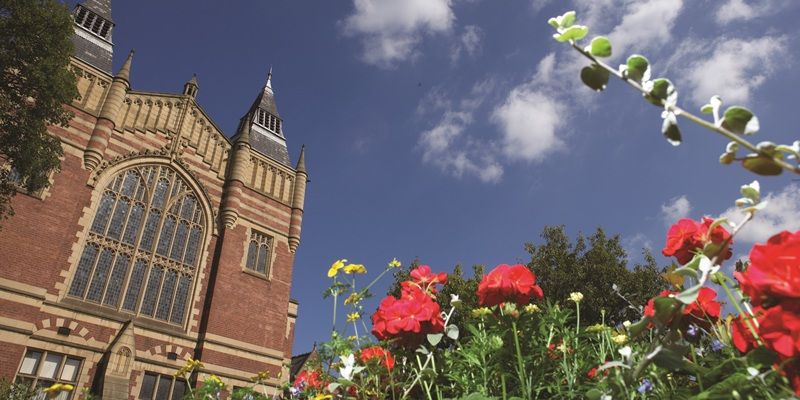 The Great Hall on a sunny day with blue sky and clouds in the background and bright flowers in the foreground.